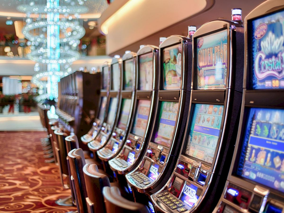 The image shows a row of slot machines in a casino, with colorful screens and a luxurious interior design including a chandelier.