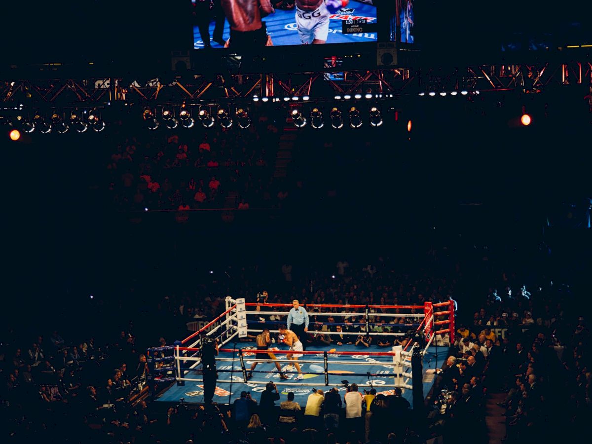 An image of a boxing match in an arena, with the fighters in the ring and spectators around. The lights illuminate the ring clearly.