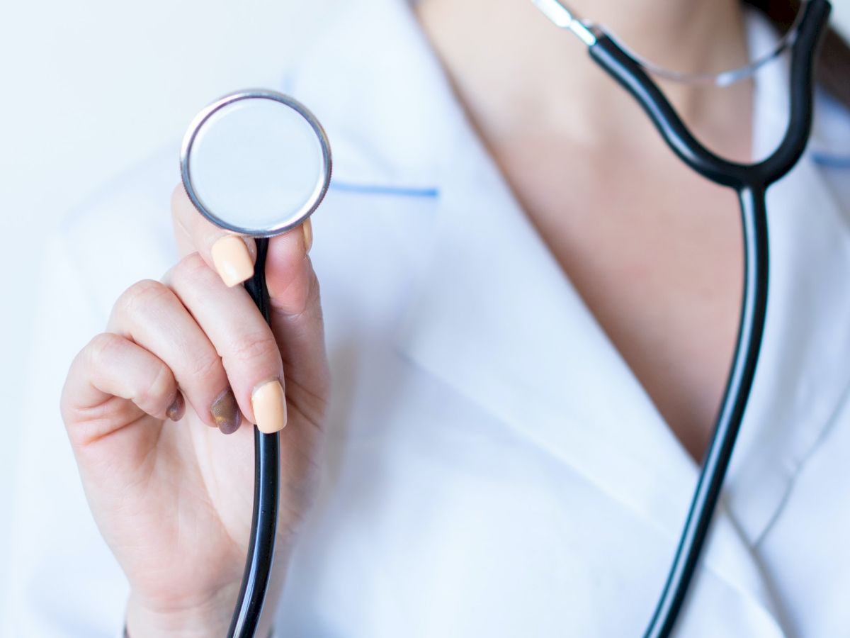 A person in a white coat is holding a stethoscope, suggesting a medical professional.