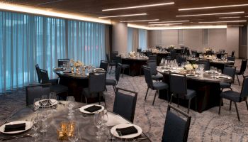 The image shows a decorated banquet hall with round tables set with dinnerware and floral centerpieces, and dim lighting creating an elegant ambiance.
