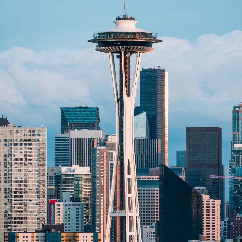 The image showcases the iconic Space Needle in Seattle, Washington, with a backdrop of the city’s diverse and towering skyline.
