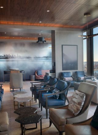 A modern lounge area with various seating arrangements, a mural on the wall, large windows showcasing a waterside view, and a Ferris wheel outside.