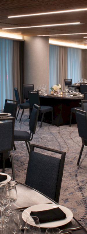 A banquet hall is set up for an event with round tables, chairs, elegant table settings, and soft lighting.