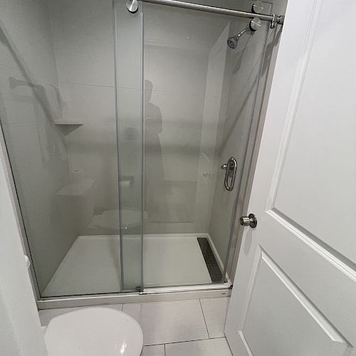 This image shows a modern bathroom featuring a glass-enclosed shower with sliding doors and a white toilet on tiled flooring.