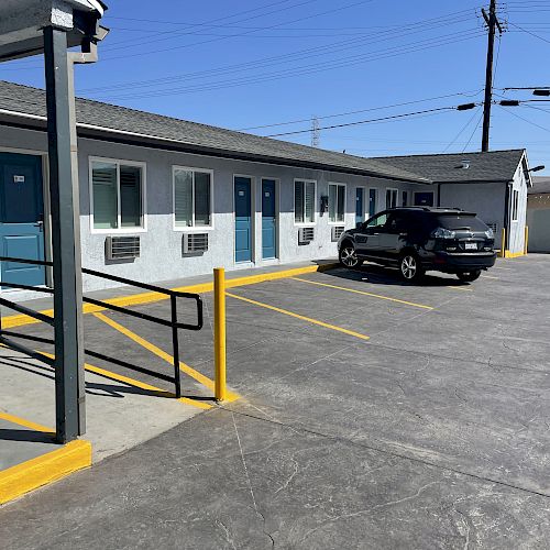 The image shows a small motel with blue doors, a black car parked in front, and yellow railing by a handicap-accessible ramp under a clear sky.