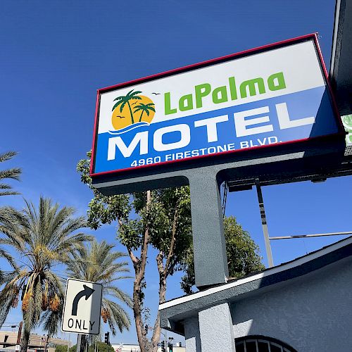 A sign for La Palma Motel at 4980 Firestone Blvd with palm trees and a clear blue sky in the background.