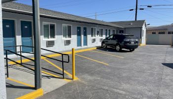 This image shows the exterior of a motel with blue doors, a single parked car, yellow parking lines, and a wheelchair-accessible ramp.