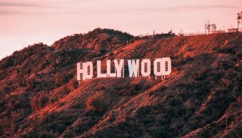 Image of the iconic Hollywood sign situated on the hills overlooking Los Angeles, captured at sunset with a pinkish hue casting over the scene.