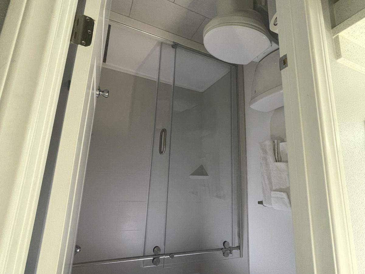 The image shows a modern bathroom with a shower enclosure, toilet, and sink, viewed from a high angle. The shower has a glass door.