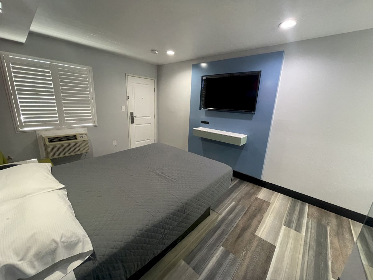 A modern, minimalist bedroom with a gray bed, wall-mounted TV, carpeted floor, window with blinds, and white-and-blue walls ends the sentence.